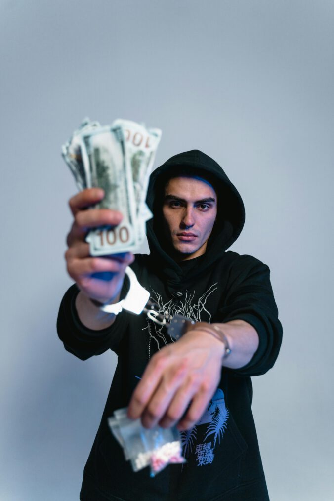 Ein Mann im Hoody hält ein Bündel Einhunderteuroscheine hoch
